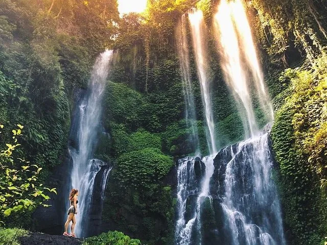 Eine Frau steht auf einem Felsen und betrachtet die zahlreichen Kaskaden des Sekumpul-Wasserfalls.