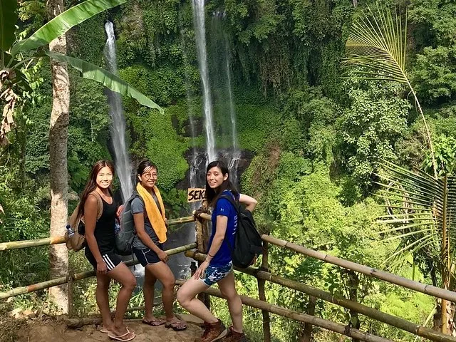 Drei lächelnde Frauen posieren auf einer Bambusplattform in der Nähe des Sekumpul-Wasserfalls.