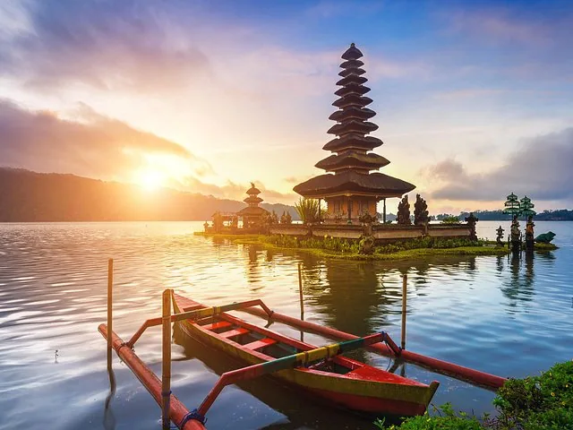 Beautiful sunrise illuminating Pura Ulun Danu Bratan temple and a wooden outrigger boat.