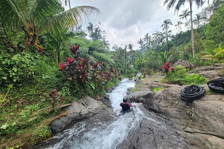 Eine Person sitzt in einem rauschenden natürlichen Wasserlauf, umgeben von leuchtenden Pflanzen.