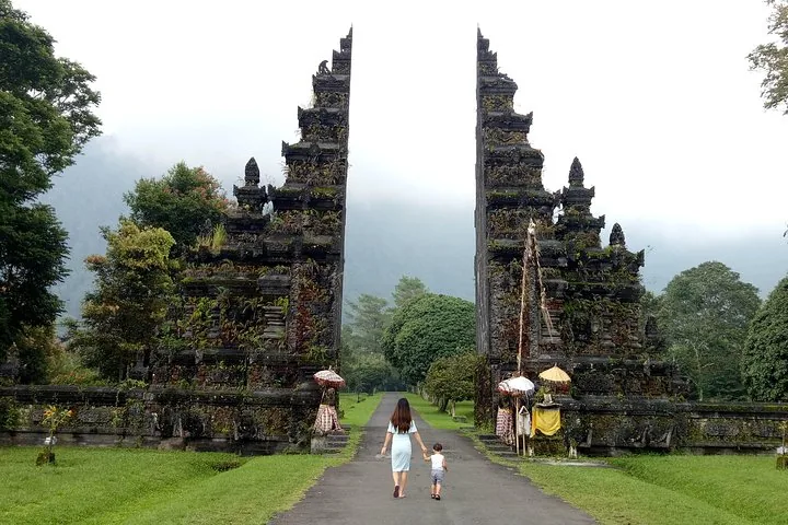 Frau und Kind gehen durch ein traditionelles gespaltenes Tor auf Bali.